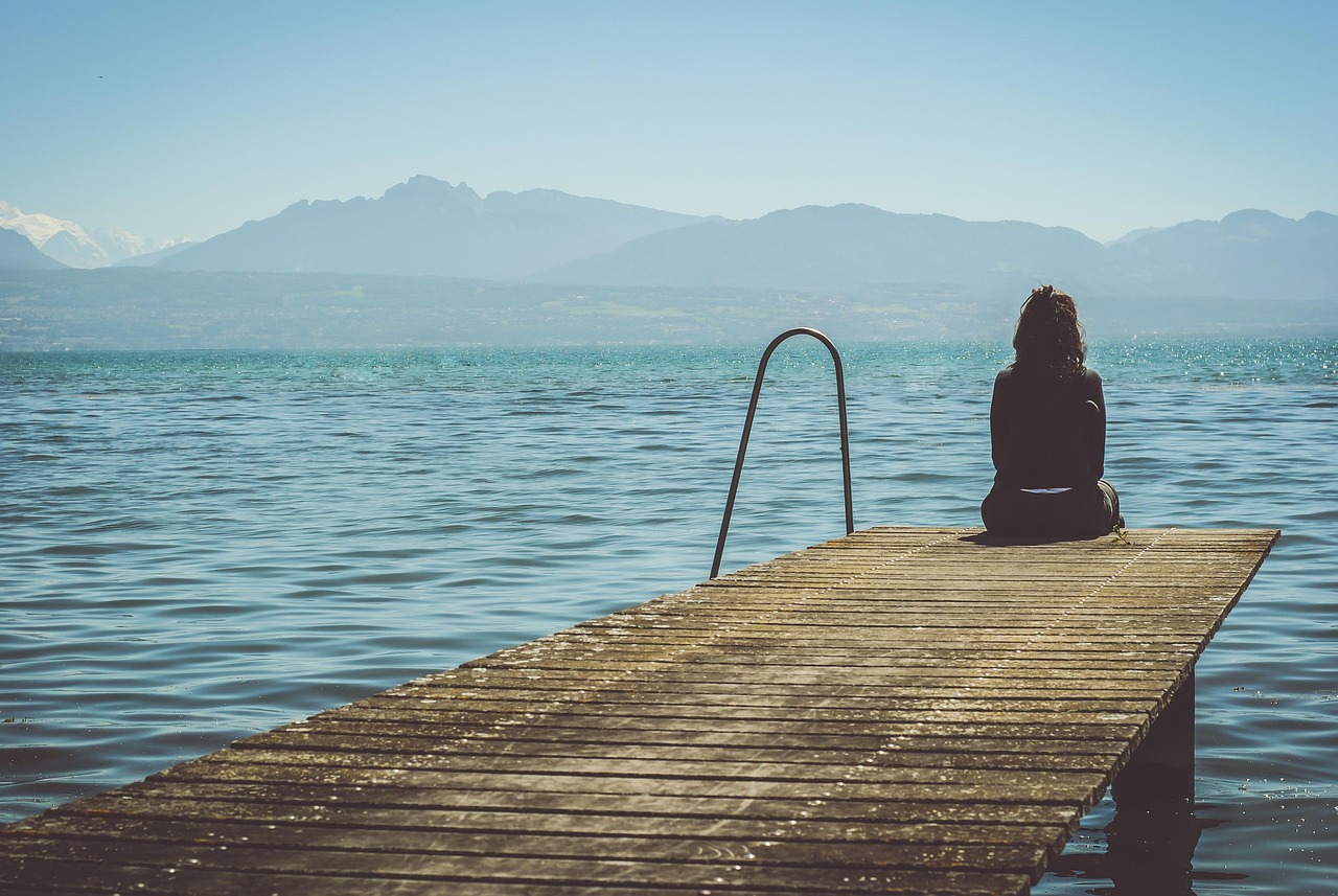 Woman sitting on the edge of a dock — symbol for when trauma survivors oull away
